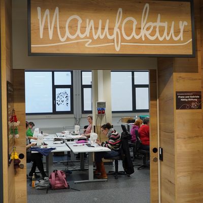 Blick in die offene Manufaktur, wo Menschen mit Behinderung an Nähmaschinen arbeiten.